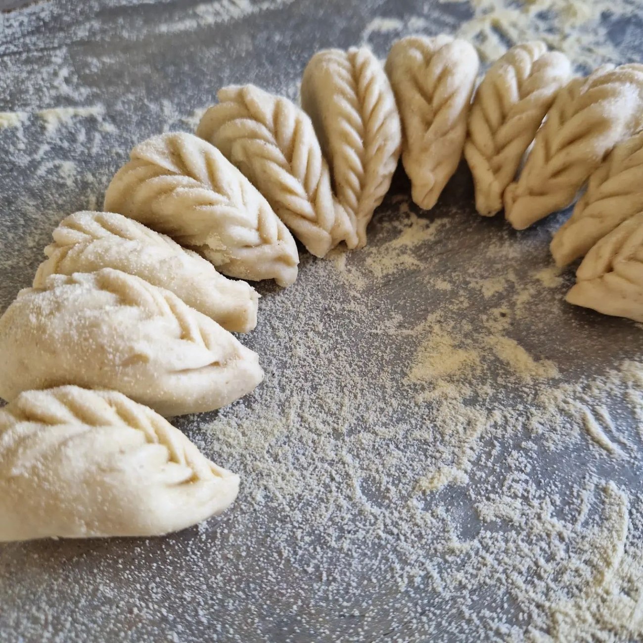 Culurgiones crudi con la chiusura a spiga disposti ad arco su un piano grigio cosparso di semola, Ristopizza da Tony