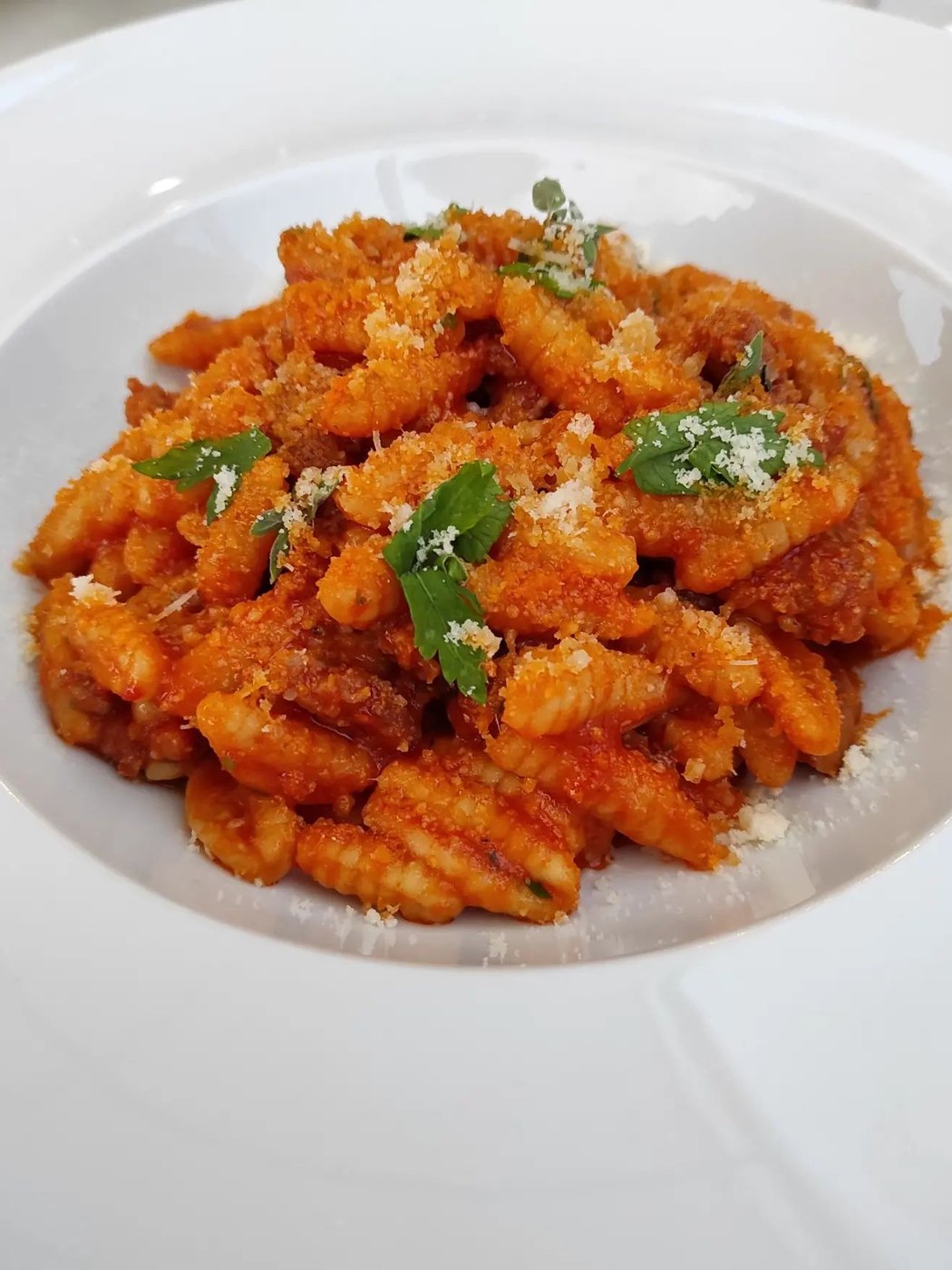 Malloreddus al ragù con formaggio grattugiato e foglie di prezzemolo in un piatto fondo bianco, Ristopizza da Tony