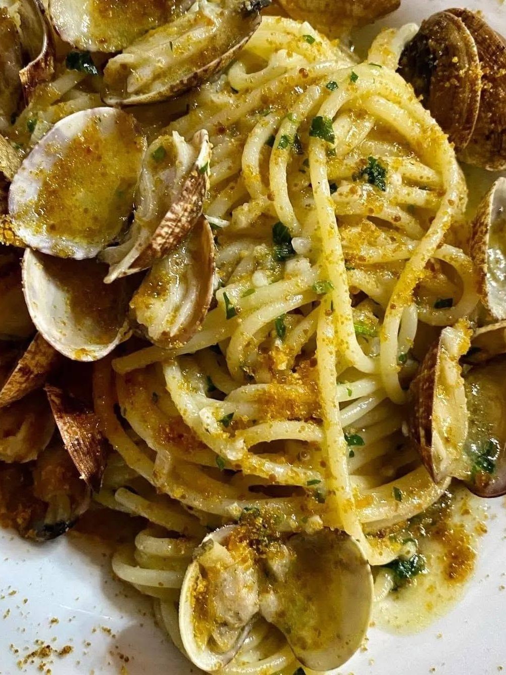 Spaghetti con vongole, bottarga grattugiata e prezzemolo tritato su un piatto bianco di Ristopizza da Tony