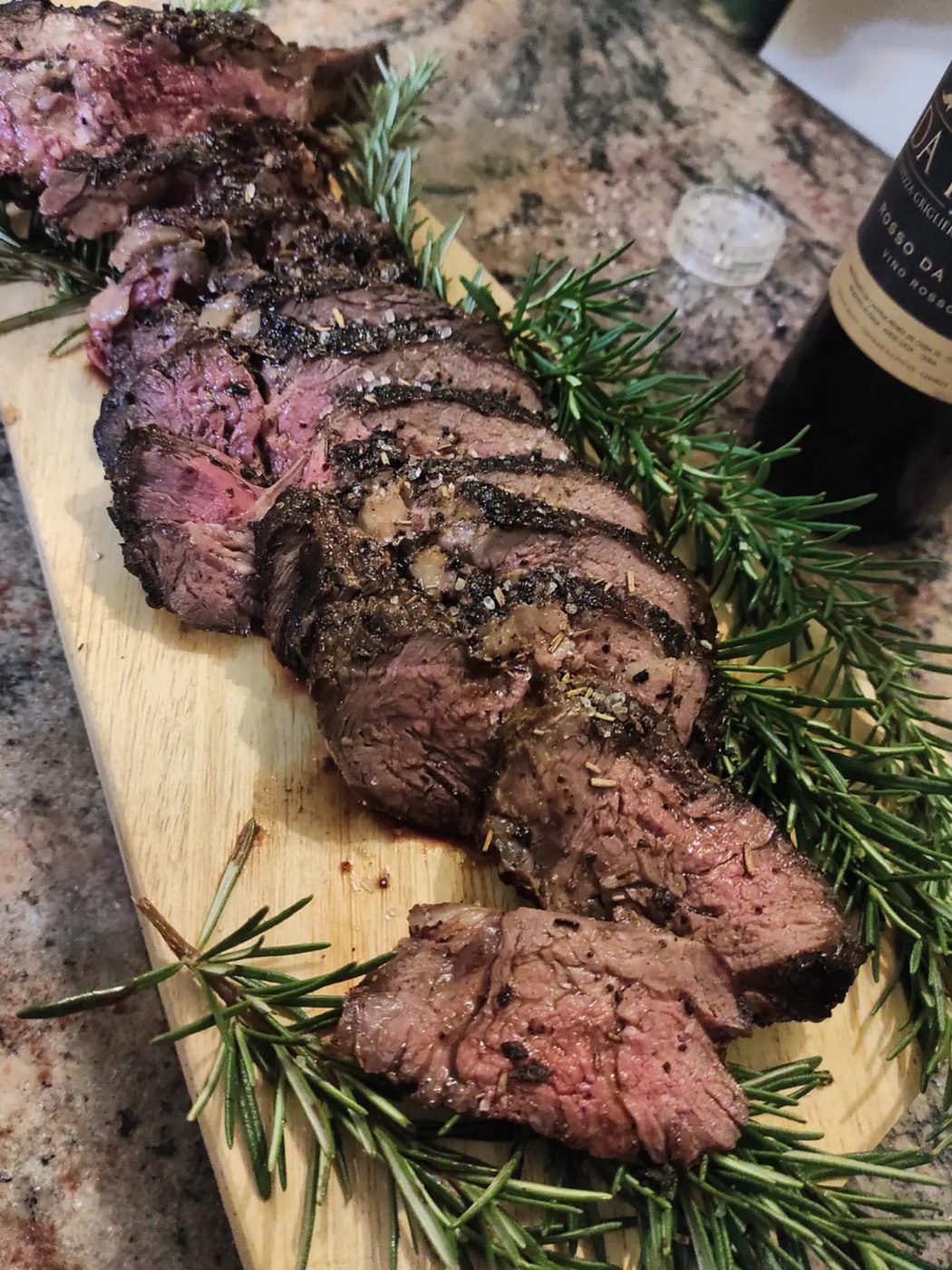 Tagliata di carne alla griglia affettata su tagliere di legno con rosmarino